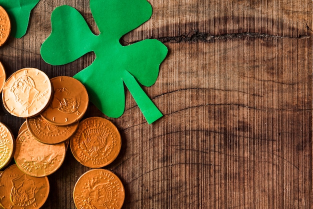 Moedas de ouro e trevos de papel na mesa de madeira