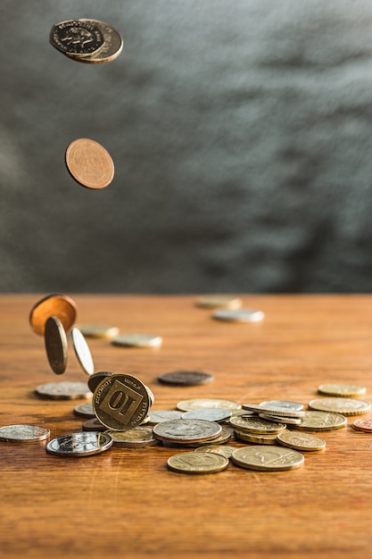 Moedas de prata e ouro e moedas caindo na mesa de madeira