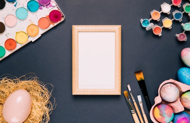 Foto grátis moldura de madeira branca com tinta aquarela; escovas e ovo de páscoa em fundo preto