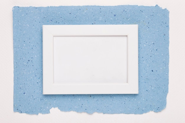Moldura vazia branca no papel azul sobre o pano de fundo branco