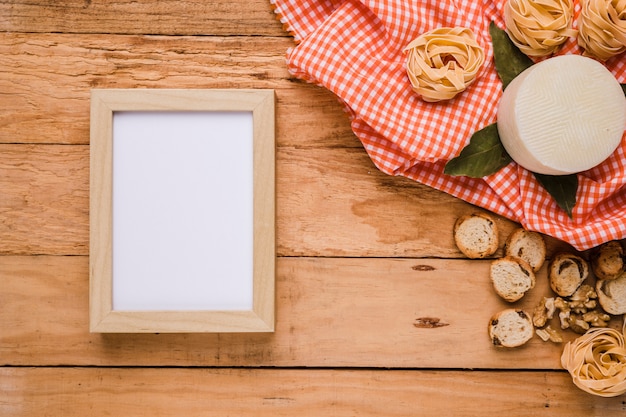 Foto grátis moldura vazia perto de comida saborosa com toalha de mesa quadriculada sobre o balcão de madeira