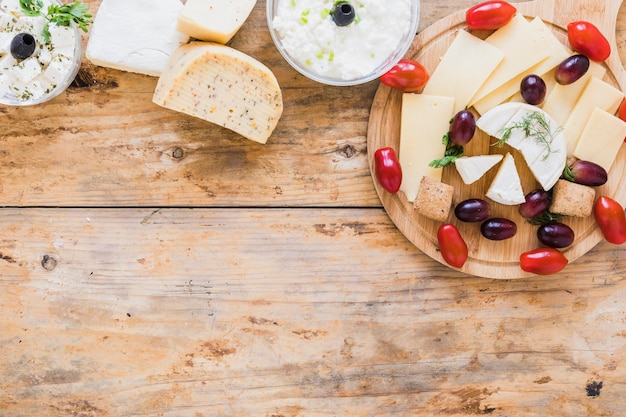 Molho de queijo e blocos com uvas e tomates na mesa de madeira