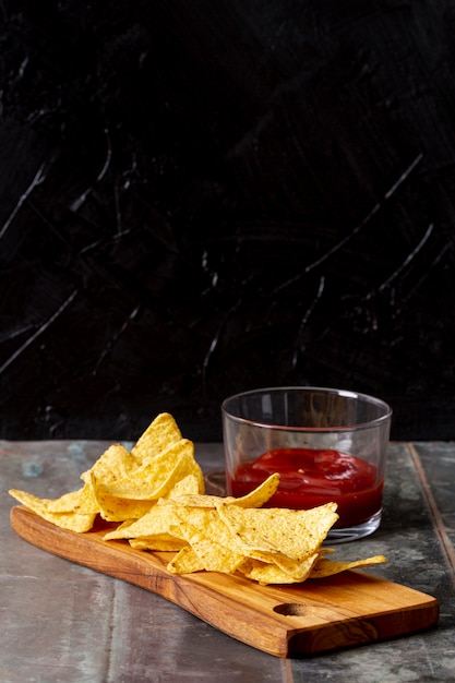 Foto grátis molho de tomate na tigela de vidro e nachos na placa de madeira