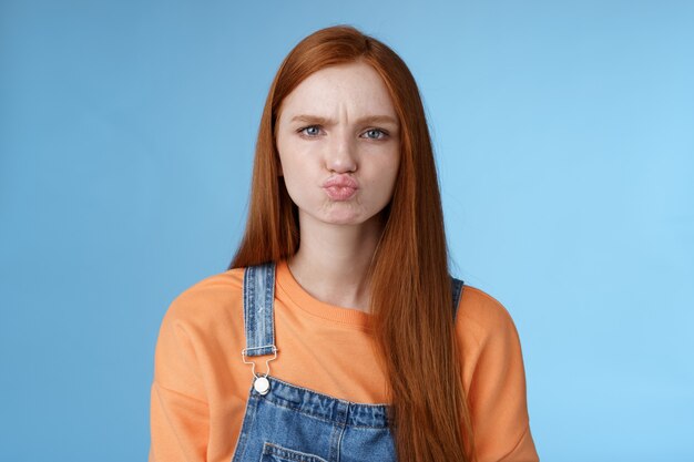 Moody desagradou namorada pegajosa ruiva olhos azuis fazendo beicinho chateado chateado ofendido franzindo a testa fazendo careta mostrando atitude em pé desapontado insatisfeito fundo azul, reclamando