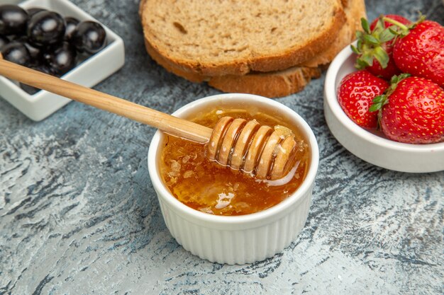 Morangos frescos com chá, pão e mel em comida doce de frutas no chão escuro.