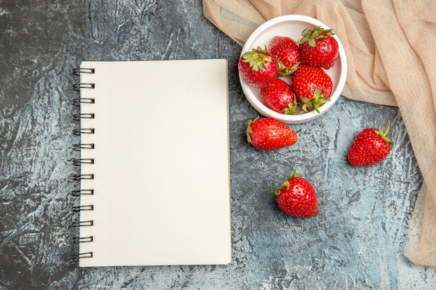 Morangos frescos e vermelhos de vista de cima com bloco de notas na superfície clara escura com frutas vermelhas