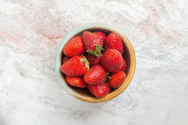 Morangos vermelhos frescos de vista de cima dentro de um pratinho na mesa branca com frutas silvestres