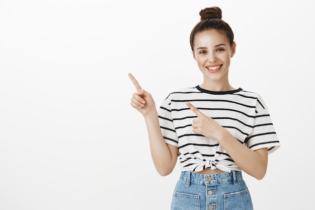 Morena atraente alegre sorrindo amplamente, apontando o dedo no canto superior esquerdo