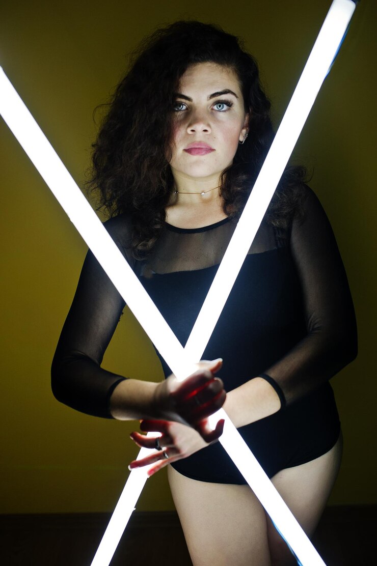 Foto grátis morena encaracolada modelo plus size com duas lâmpadas led longas contra a parede amarela