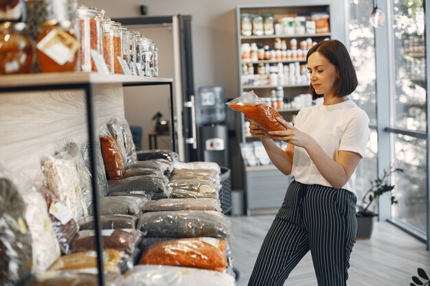 Morena escolhe comida. A senhora está segurando frutas secas. Menina com uma camisa branca no supermercado.