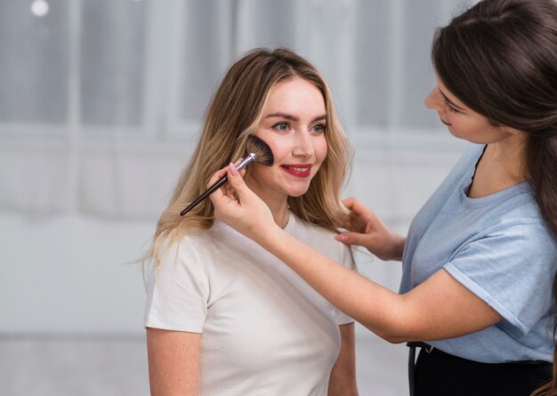 Morena fazendo maquiagem para mulher sorridente