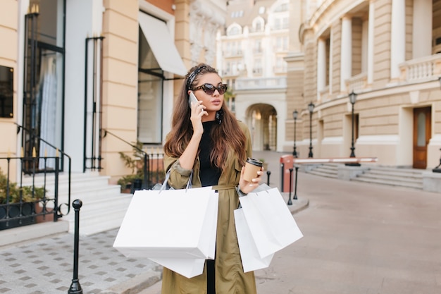 Morena séria e fashionista falando ao telefone durante as compras no fim de semana de outono