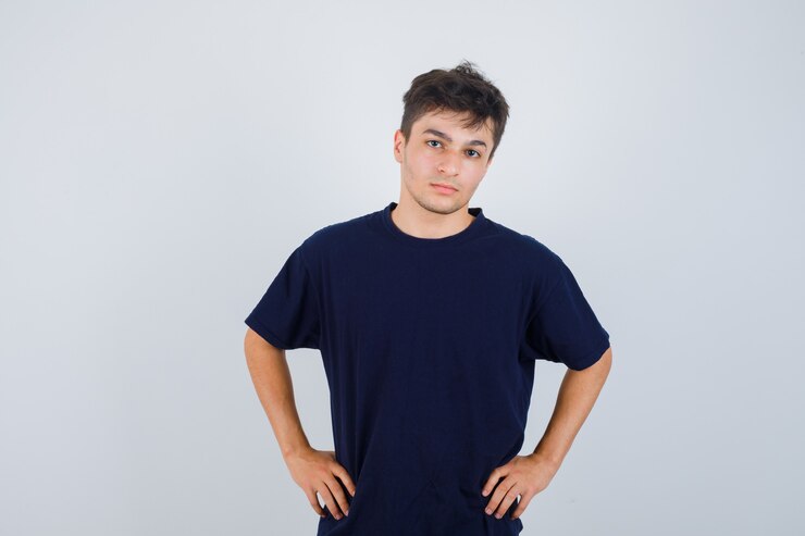 Foto grátis moreno homem em t-shirt escura, olhando para a câmera, mantém as mãos na cintura e olhando sério, vista frontal.