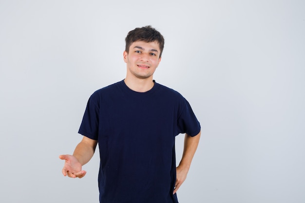 Moreno homem esticando a mão em um gesto de questionamento em t-shirt e olhando alegre, vista frontal.