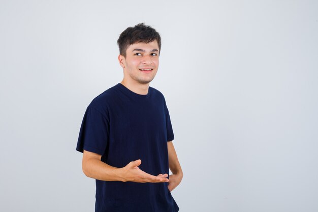 Moreno homem fingindo mostrar algo em t-shirt e olhando alegre, vista frontal.