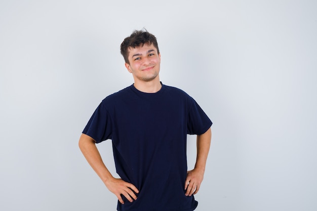 Foto grátis moreno homem segurando as mãos na cintura em uma camiseta escura e olhando bonito, vista frontal.