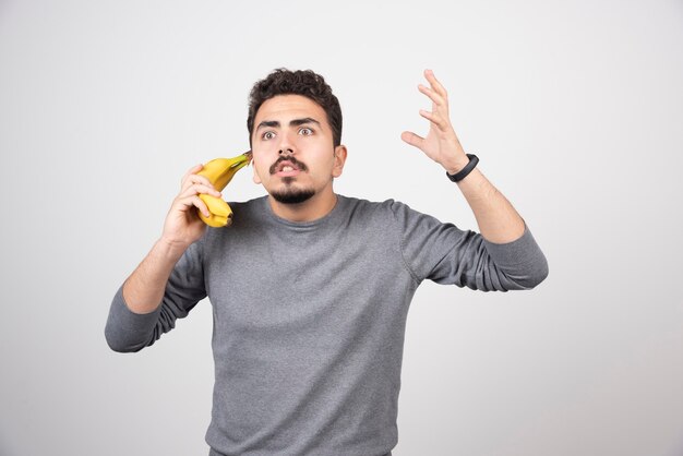 Moreno macho segurando banana como um telefone.