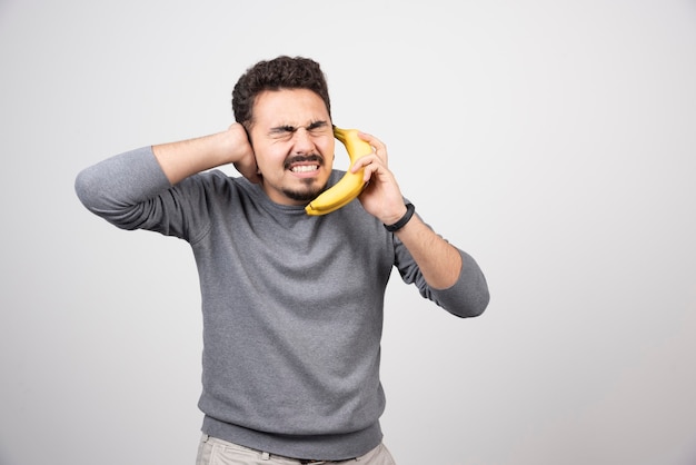 Moreno macho segurando banana como um telefone.