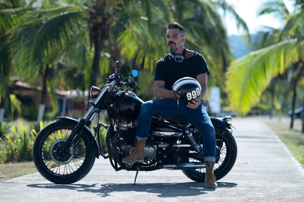 Motociclista com barba espessa posa em uma motocicleta em um belo parque