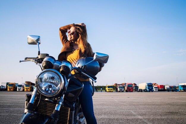 Motociclista feminina em uma jaqueta de couro, sentada em uma moto retrô e sorrindo