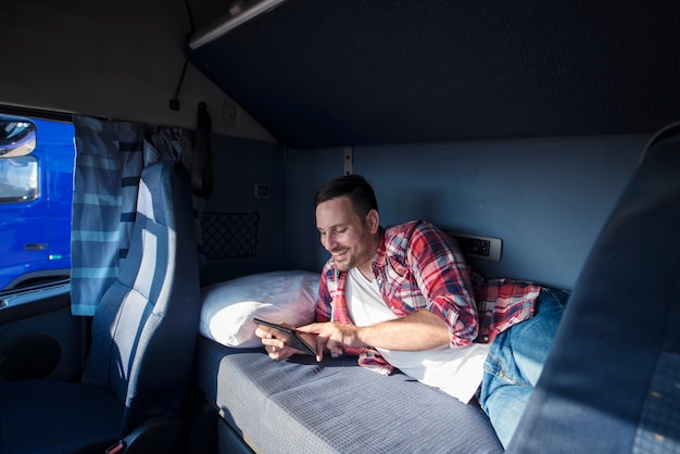 Motorista de caminhão deitado na cama em sua cabine se comunicando com sua família por meio do computador tablet