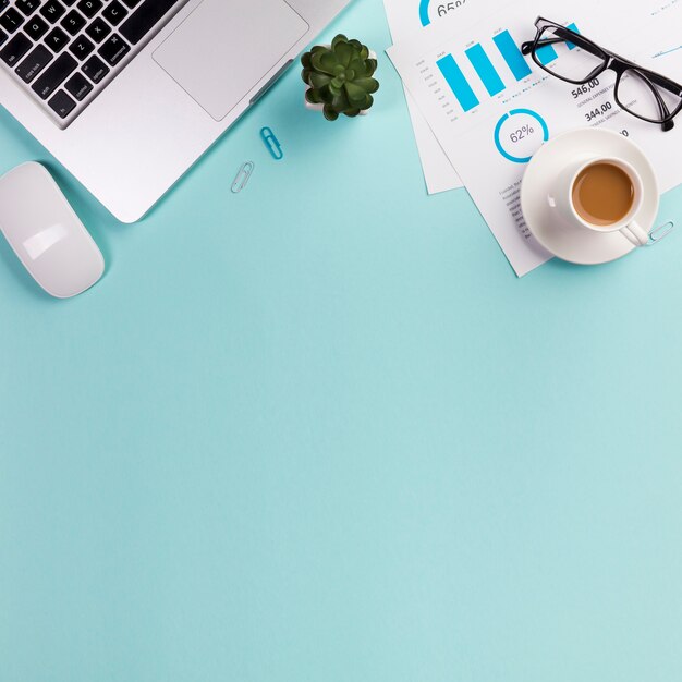 Mouse, laptop, planta do cacto, óculos, plano de orçamento e xícara de café sobre fundo azul