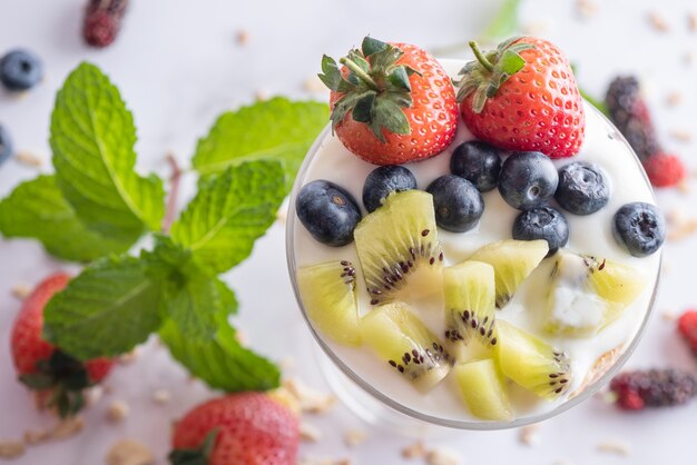 Muesli caseiro, tigela de granola de aveia com iogurte, mirtilos frescos, amora, morangos, kiwi, hortelã e placa de nozes para café da manhã saudável, copie o espaço. Conceito de pequeno-almoço saudável. Comer limpo.