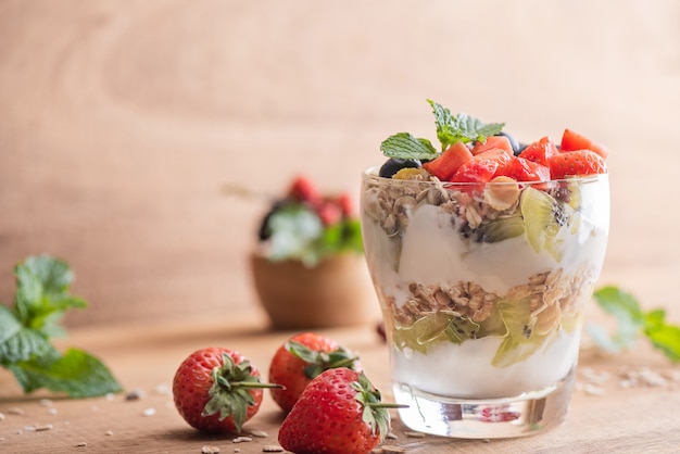 Muesli caseiro, tigela de granola de aveia com iogurte, mirtilos frescos, amora, morangos, kiwi, hortelã e placa de nozes para café da manhã saudável, copie o espaço. Conceito de pequeno-almoço saudável. Comer limpo.