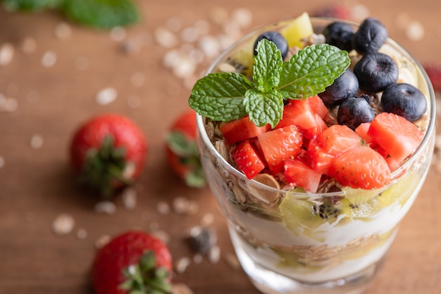 Muesli caseiro, tigela de granola de aveia com iogurte, mirtilos frescos, amora, morangos, kiwi, hortelã e placa de nozes para café da manhã saudável, copie o espaço. Conceito de pequeno-almoço saudável. Comer limpo.