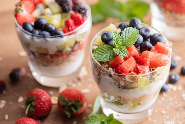 Muesli caseiro, tigela de granola de aveia com iogurte, mirtilos frescos, amora, morangos, kiwi, hortelã e placa de nozes para café da manhã saudável, copie o espaço. Conceito de pequeno-almoço saudável. Comer limpo.