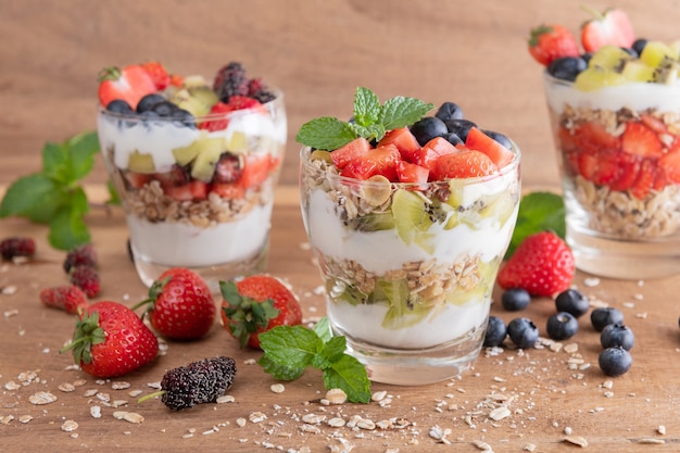 Muesli caseiro, tigela de granola de aveia com iogurte, mirtilos frescos, amora, morangos, kiwi, hortelã e placa de nozes para café da manhã saudável, copie o espaço. Conceito de pequeno-almoço saudável. Comer limpo.