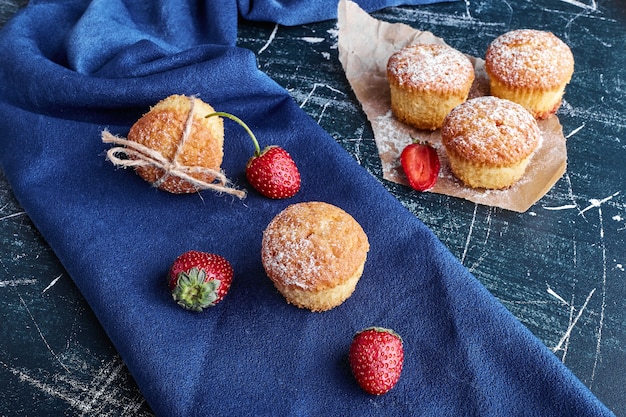 Muffins com morangos na superfície azul.