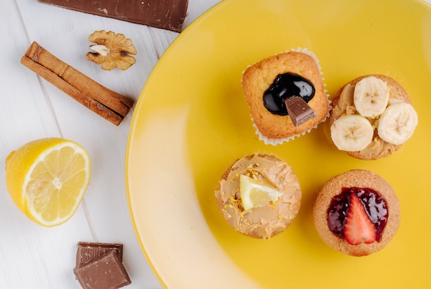 Muffins de vista superior com morangos bananas chocolate e limão num prato amarelo com canela