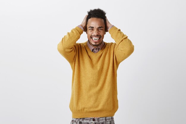 Foto grátis muita dor para uma cabeça. retrato de um afro-americano atraente e desconfortável, de suéter amarelo, segurando as mãos no cabelo, fazendo careta e apertando os olhos, sentindo desconforto e dor de cabeça