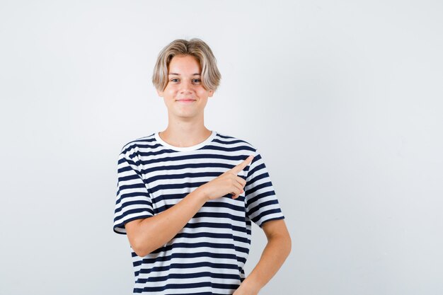 Muito adolescente em t-shirt listrada, apontando para o canto superior direito e olhando alegre, vista frontal.