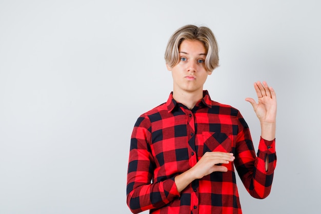 Muito adolescente, mostrando o sinal de tamanho pequeno em uma camisa xadrez e olhando hesitantemente, vista frontal.