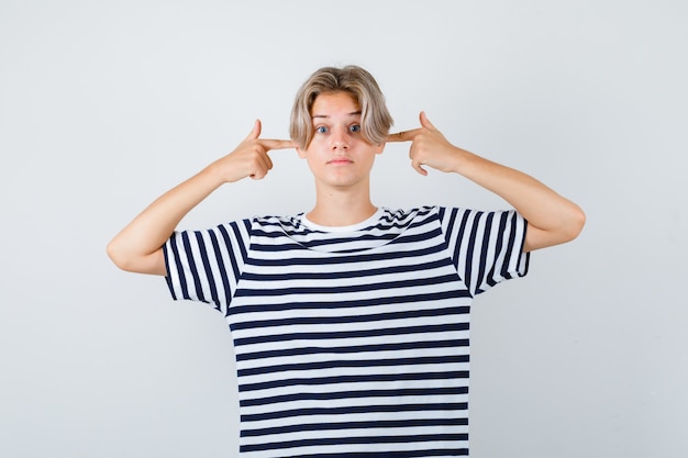 Muito adolescente tampando as orelhas com os dedos em uma camiseta listrada e parecendo confuso, vista frontal.