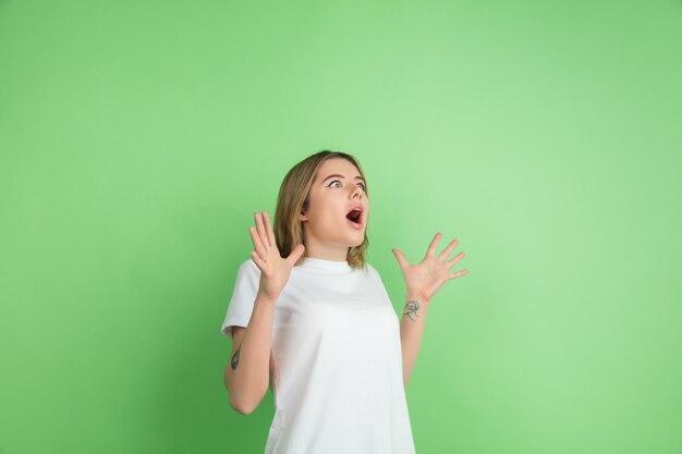 Muito chocado. Retrato de mulher jovem branca isolado na parede verde do estúdio.