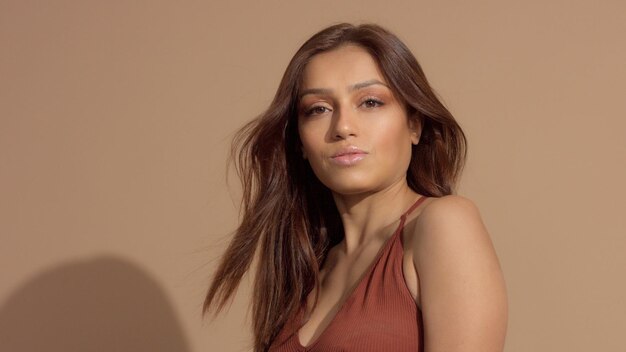 Muito jovem modelo em estúdio sorrindo e assistindo ao cabelo da câmera soprando sombras brilhantes
