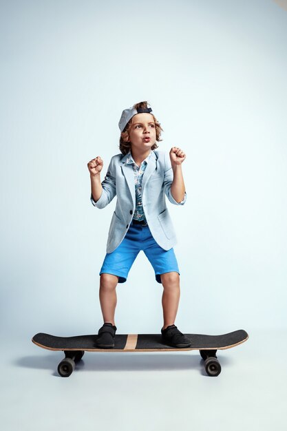 Muito jovem num skate com roupas casuais na parede branca do estúdio