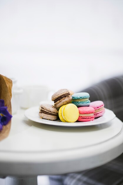 Muitos macaroons coloridos na placa cerâmica branca sobre a mesa