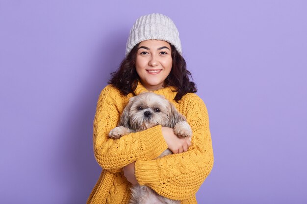 Mulher abraçando seu cachorrinho e olhando diretamente para a câmera com uma expressão facial satisfeita