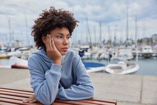 Mulher admira iates e a água do mar calma passa o tempo livre no cais do porto vestida com um moletom sonha com a viagem de verão nas férias sai após a quarentena