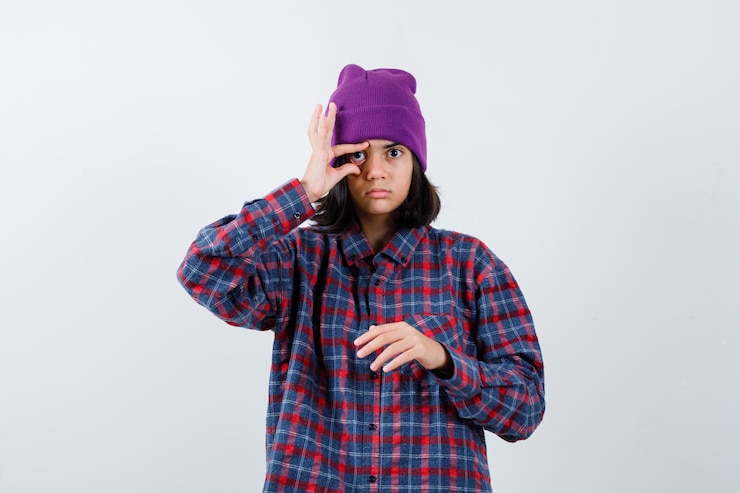 Foto grátis mulher adolescente abrindo os olhos com os dedos em uma camisa xadrez e um gorro