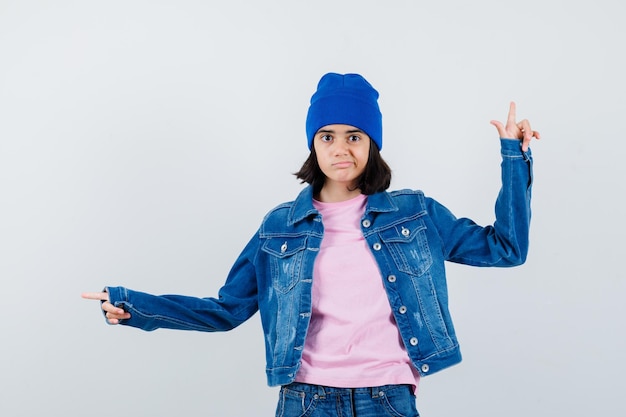 Mulher adolescente com camiseta rosa apontando para cima e para a esquerda com os dedos indicadores, parecendo séria