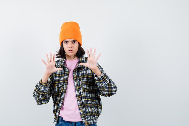 Mulher adolescente de camisa xadrez e gorro gesticulando isolada