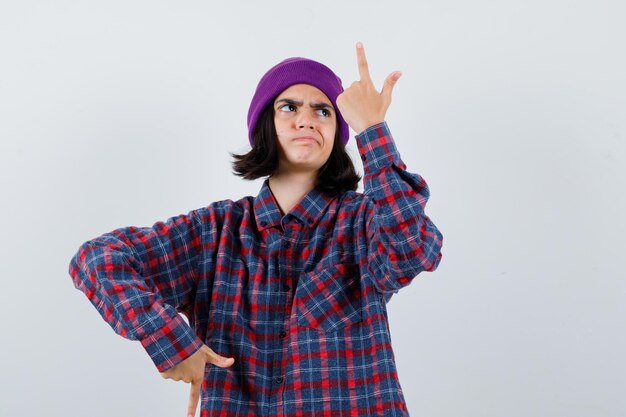 Mulher adolescente de camisa xadrez e gorro gesticulando isolada