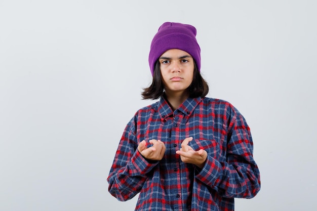 Mulher adolescente de camisa xadrez e gorro gesticulando isolada