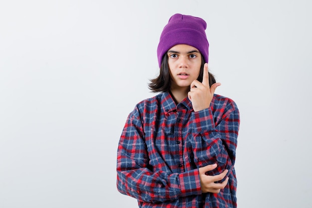 Mulher adolescente de camisa xadrez e gorro gesticulando isolada