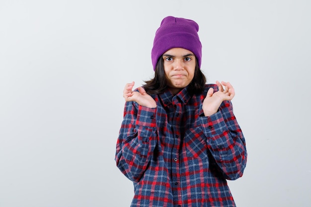 Mulher adolescente de camisa xadrez e gorro gesticulando isolada